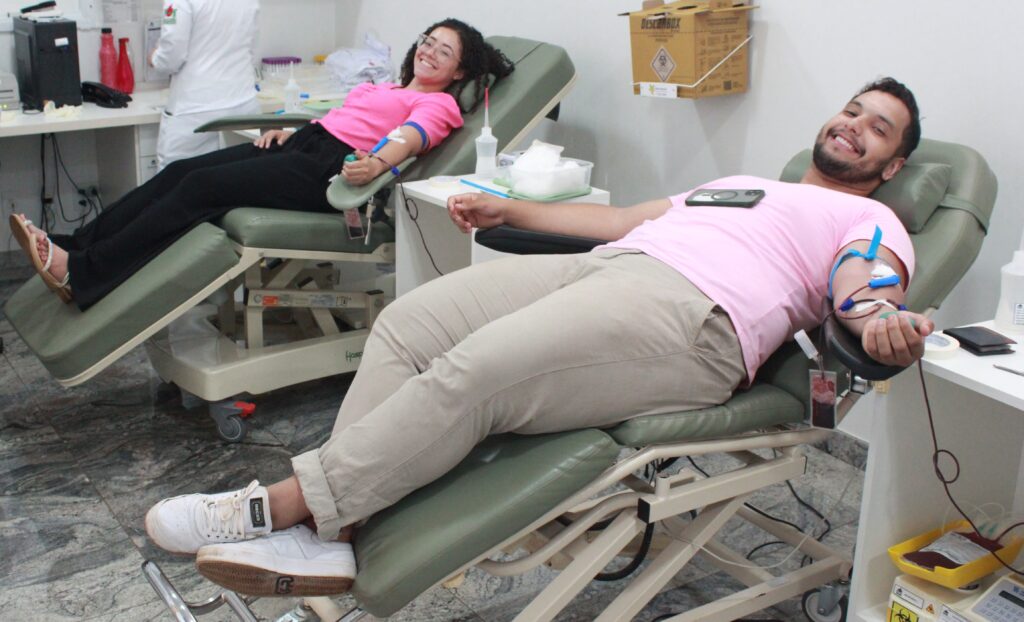 Foto colorida mostra dois jovens doando sangue.